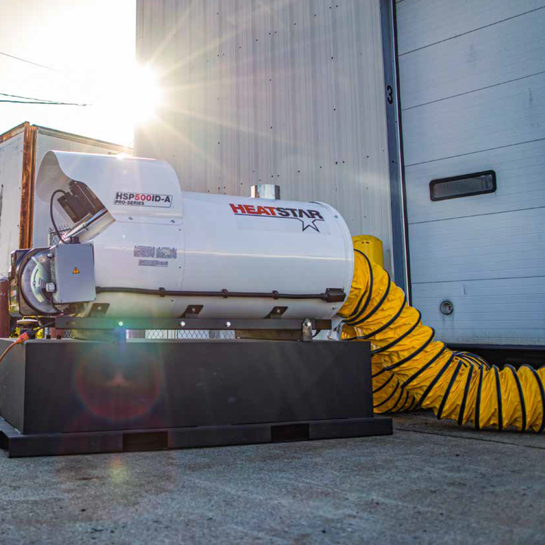 A Heatstar indirect fired heating system on a black base, connected to a yellow flexible duct, photographed outdoors in front of a white industrial building door.